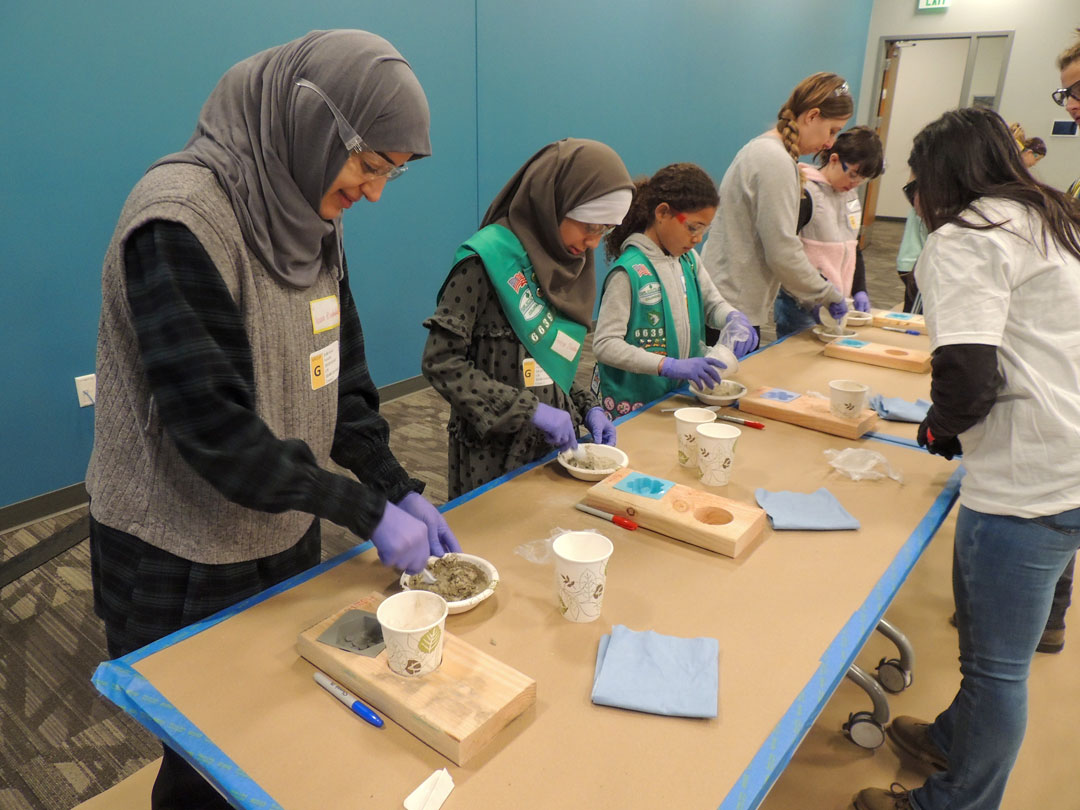 Girl Scouts and volunteers casting concrete stepping stones at a workshop table