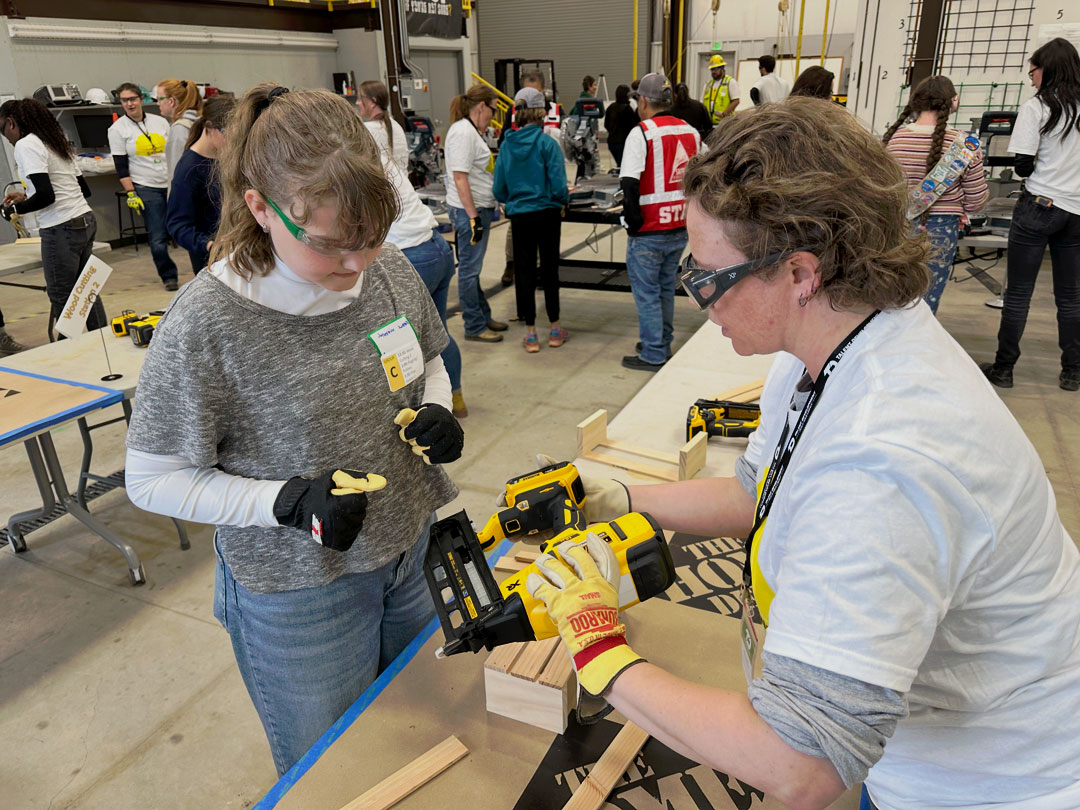 A volunteer showing a Girl Scout how to use a nail gun