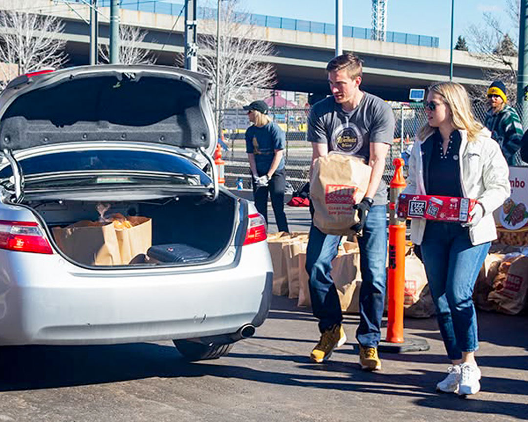 Volunteers carrying groceries to a car trunk at a mobile food bank site