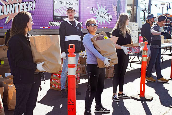 Volunteers carrying bags of groceries past a Food Bank of the Rockies truck