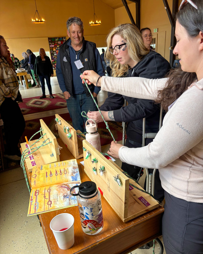 Staff members practicing knot-tying at a retreat activity station