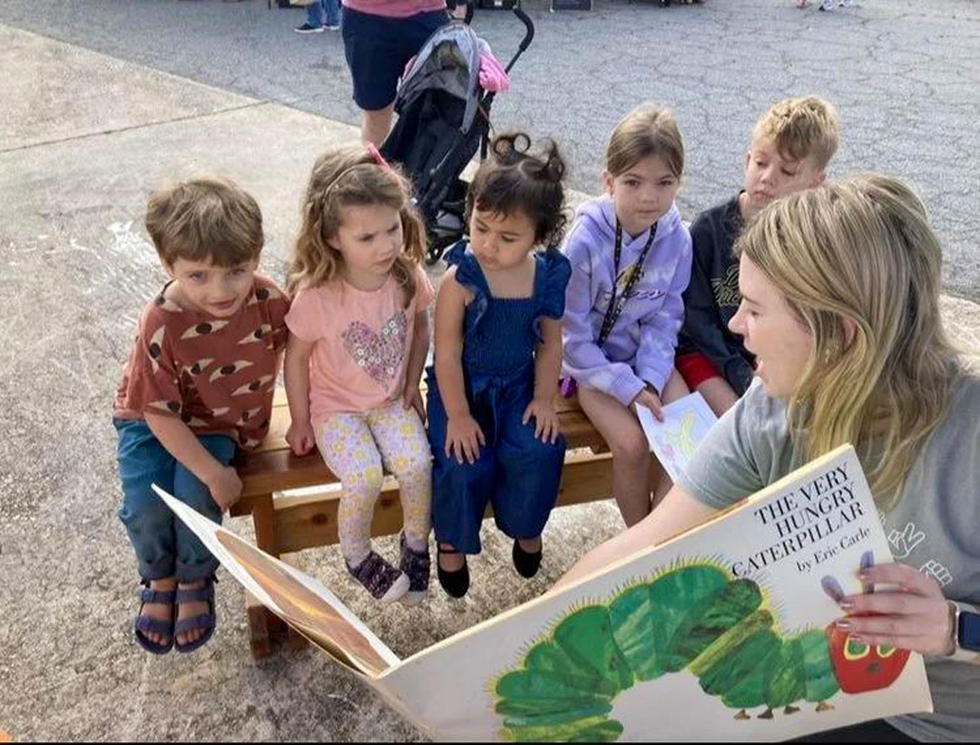 A reader sharing The Very Hungry Caterpillar with children outdoors